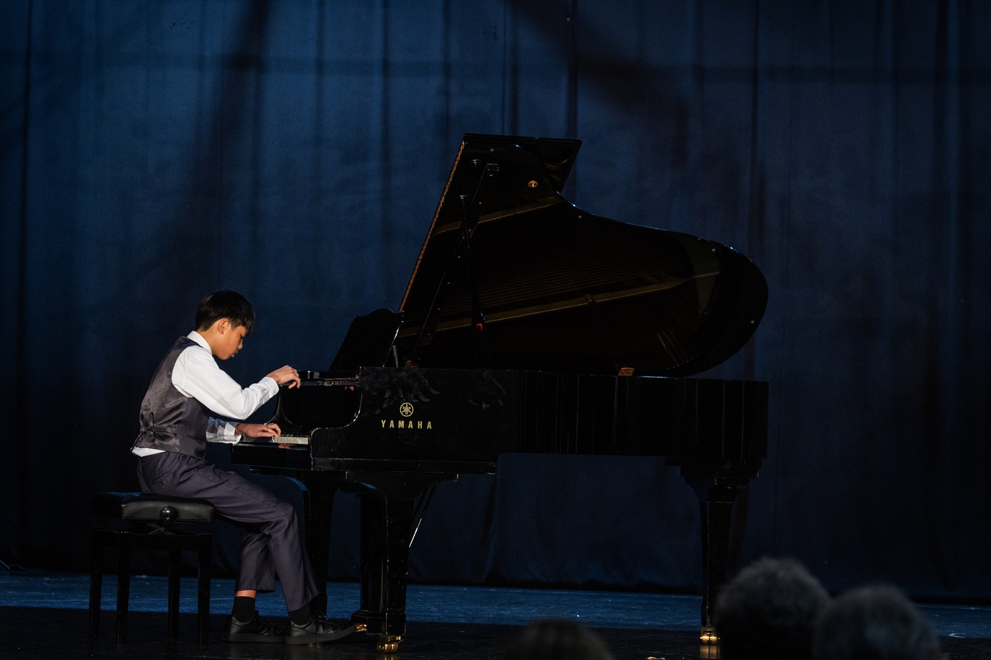 A young pianist performs on the Festival stage, lit by a single spotlight.
