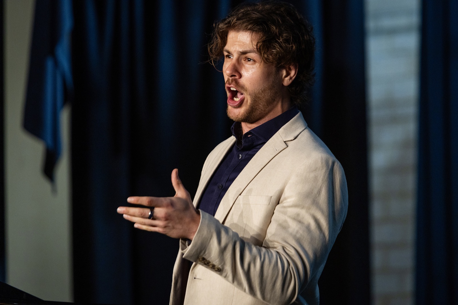 A tenor mid-phrase during a Festival Session, warmly lit against a dark stage curtain.