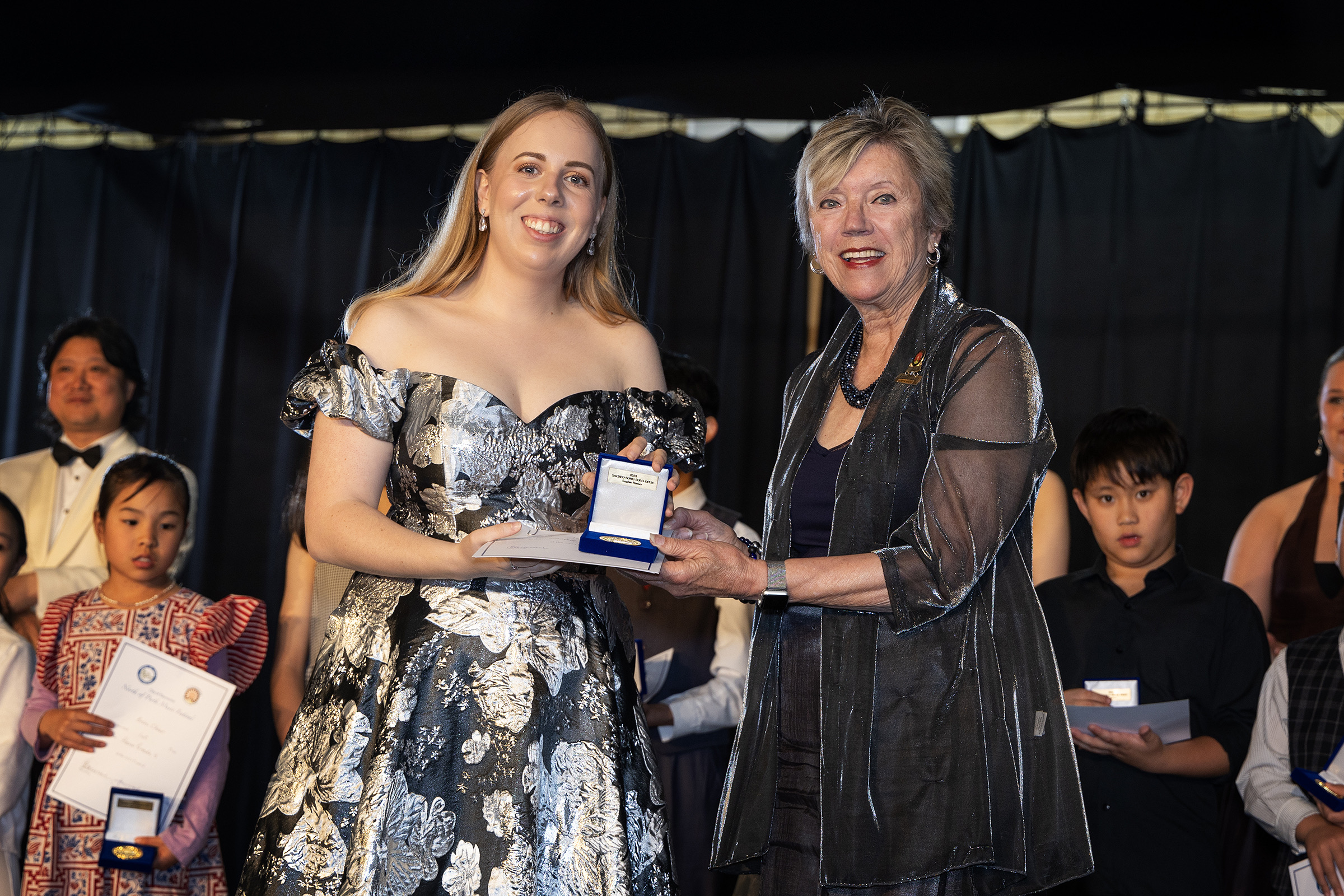 A senior winner in a formal gown receives her award from a presenter.