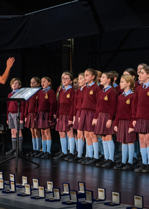 A choir performs, with medallion boxes lined up in front of the stage.