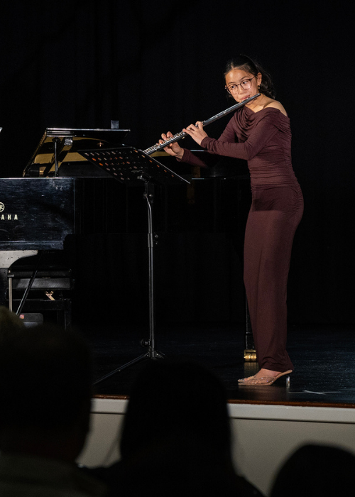 A flautist performs a solo beside a grand piano.
