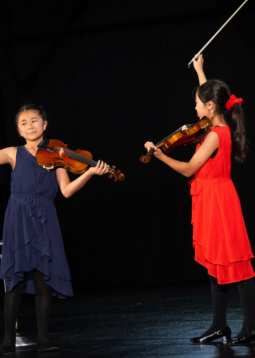 Two young violinists perform a duet.
