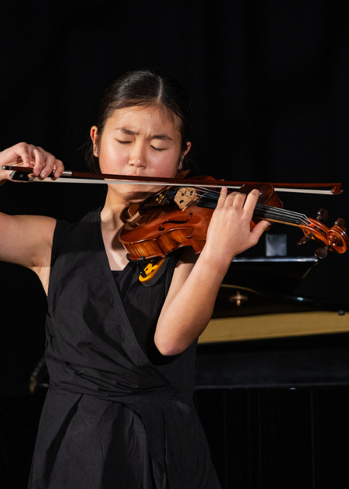 A violinist performs a solo, eyes closed in concentration.