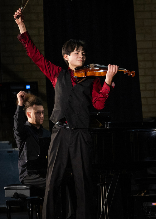 A violinist raises his bow at the end of a triumphant performance.