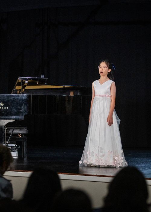 A young vocalist performs beside a grand piano.
